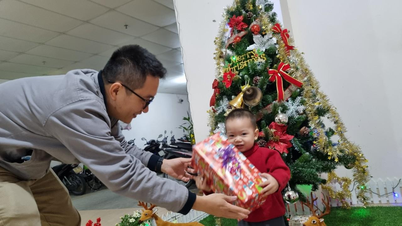 Em bé thích thú khi được ôm hộp quà, tạo dáng chụp ảnh trước cây thông Noel.