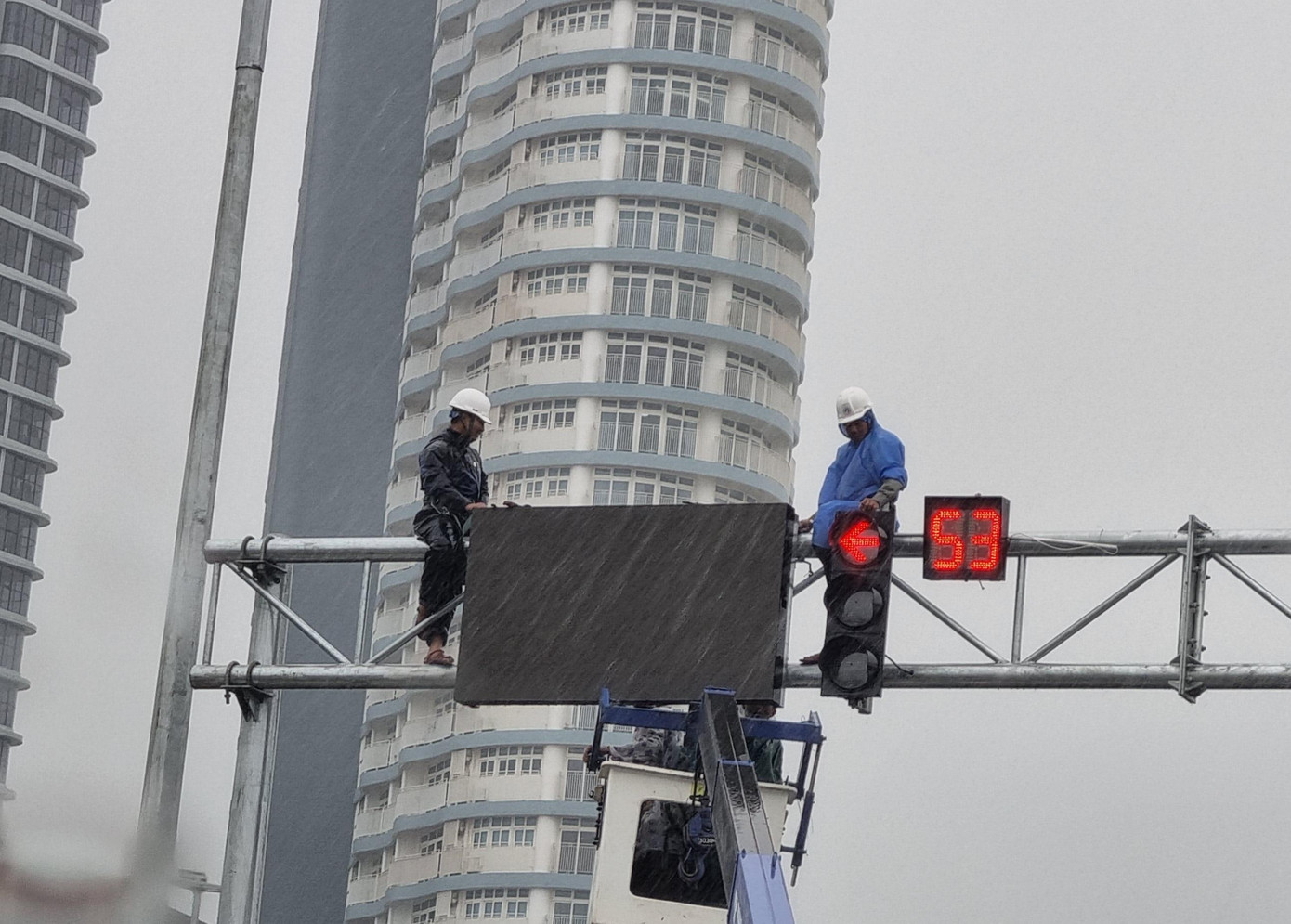 Các công nhân được xe nâng đưa lên cột, mưa gió táp thẳng vào mặt. Một công nhân cho hay cả đội có mặt từ trưa đến cuối chiều để sửa chữa trên bốn cột đèn giao thông ngay nút giao này.
