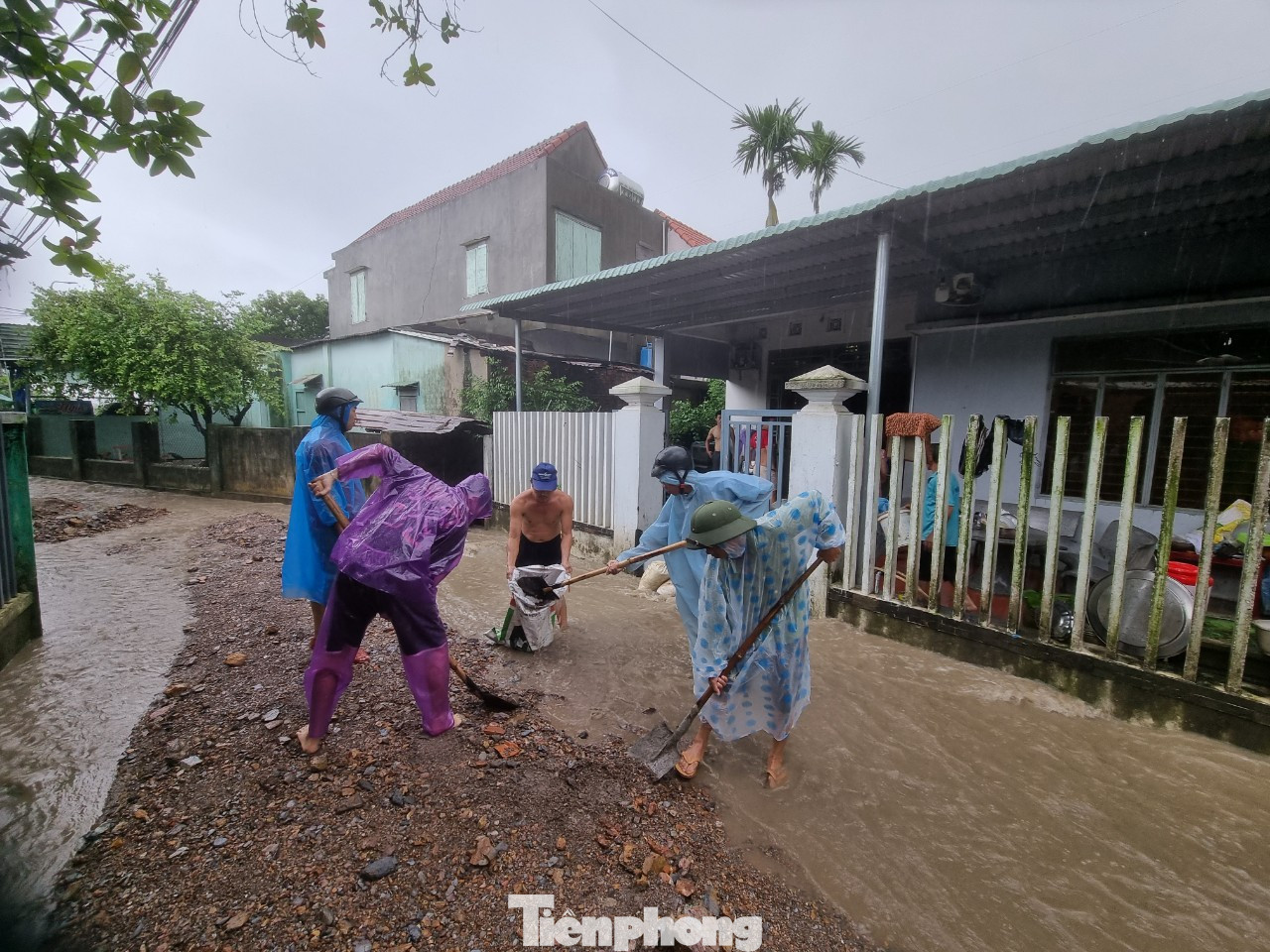 Bà con đội mưa xúc đất đá vào bao cát làm kè chắn ngay trước cổng để chặn bùn tuồn vào bên trong nhà.
