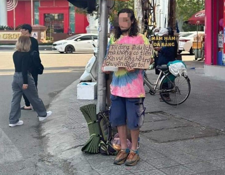 Nam du khách đứng giữa phố cầm bảng xin tiền.