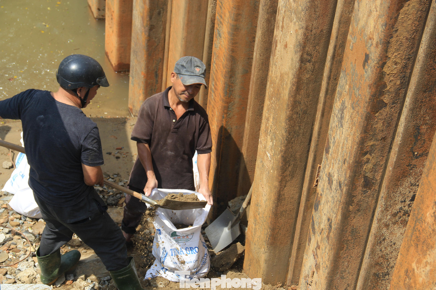 Công nhân múc cát vào bao, tạo một kè tạm để đất đá khỏi bị trôi tuột.