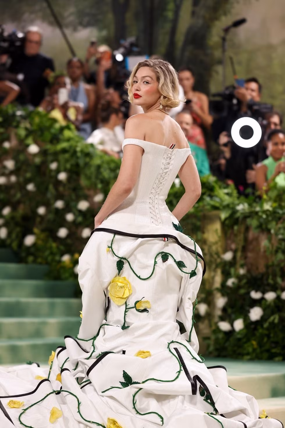 Gigi Hadid mặc váy trễ vai với đuôi cá bồng bềnh chất liệu lụa moiré, phần viền bằng sa tanh duchesse màu đen được trang trí bằng hoa hồng vàng 3D. Từng chi tiết nhỏ của bộ đầm được 70 người thợ thực hiện tỉ mỉ bằng tay trong hơn 13.500 giờ đồng hồ. Chỉ riêng phần đuôi váy bồng bềnh đã khiến phải sử dụng đội thợ 40 người trong 8.500 giờ để thêu.