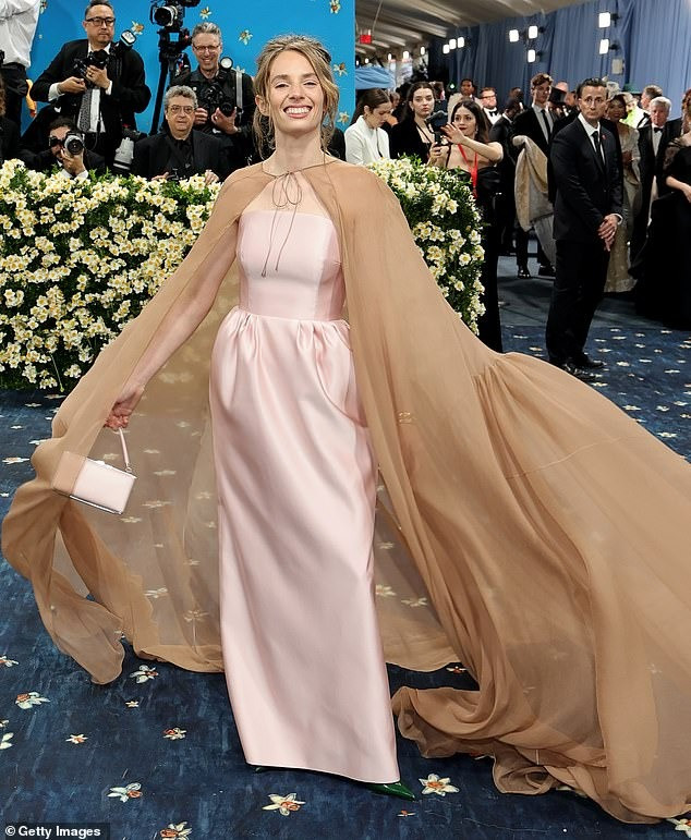 Maya Hawke mặc đầm lụa hồng nhạt của Prada với corset đi kèm áo choàng nâu. Dải nơ buộc phía trước lỏng lẻo tạo cảm giác luộm thuộm, không phù hợp với sự kiện.