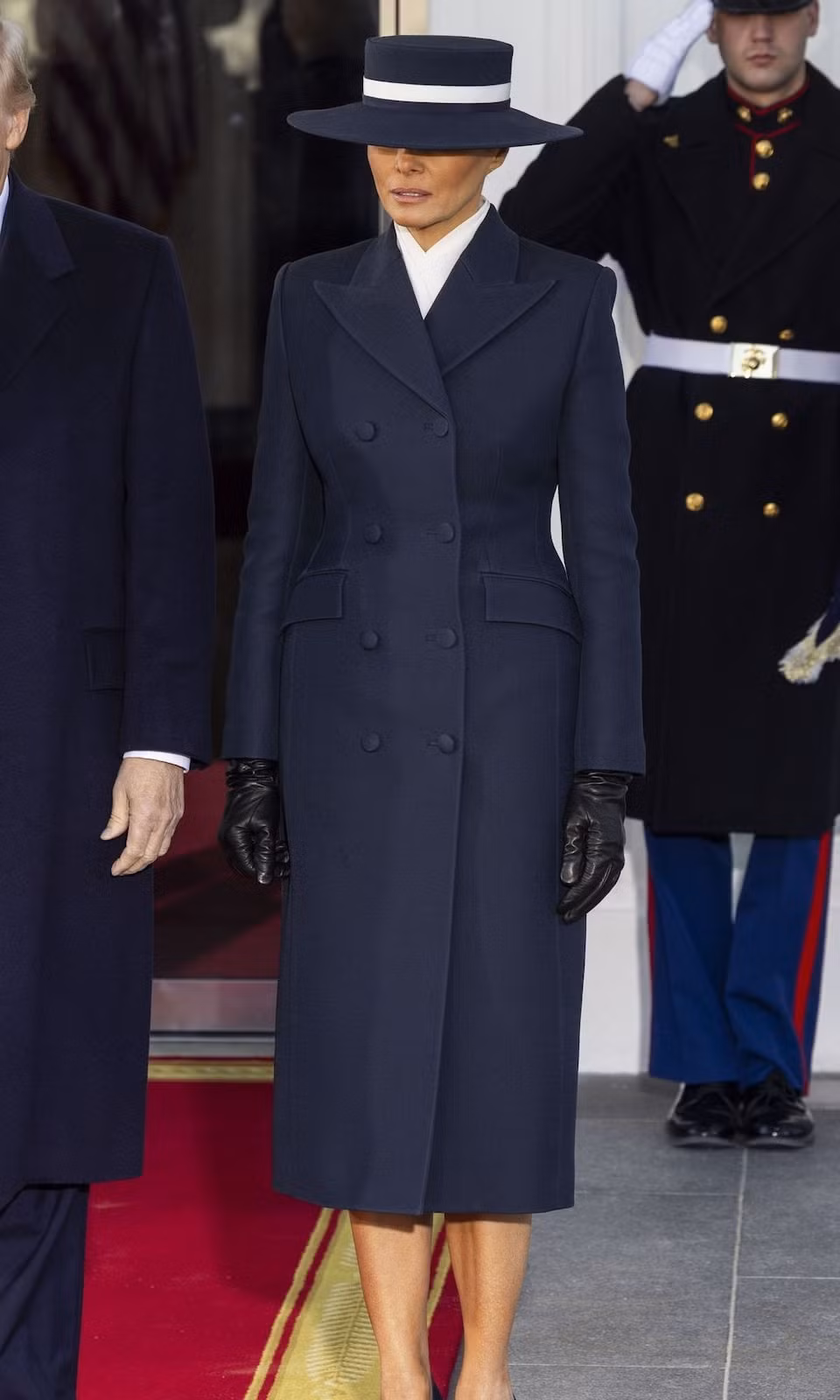 Trong sự kiện này, Melania Trump đã chọn bộ trang phục tông xanh navy đồng nhất, thể hiện rõ nét thanh lịch và gu thẩm mỹ tinh tế không thể nhầm lẫn. Tân Đệ nhất phu nhân chọn chiếc áo khoác dáng dài hai hàng cúc của Adam Lippes, kết hợp hoàn hảo với chiếc mũ rộng vành được thiết kế bởi Eric Javits. Hoàn thiện vẻ ngoài là đôi giày cao gót Manolo Blahnik màu navy, găng tay da đen và chiếc áo sơ mi trắng thoáng lộ ở cổ, tạo điểm nhấn cổ điển, tinh tế.