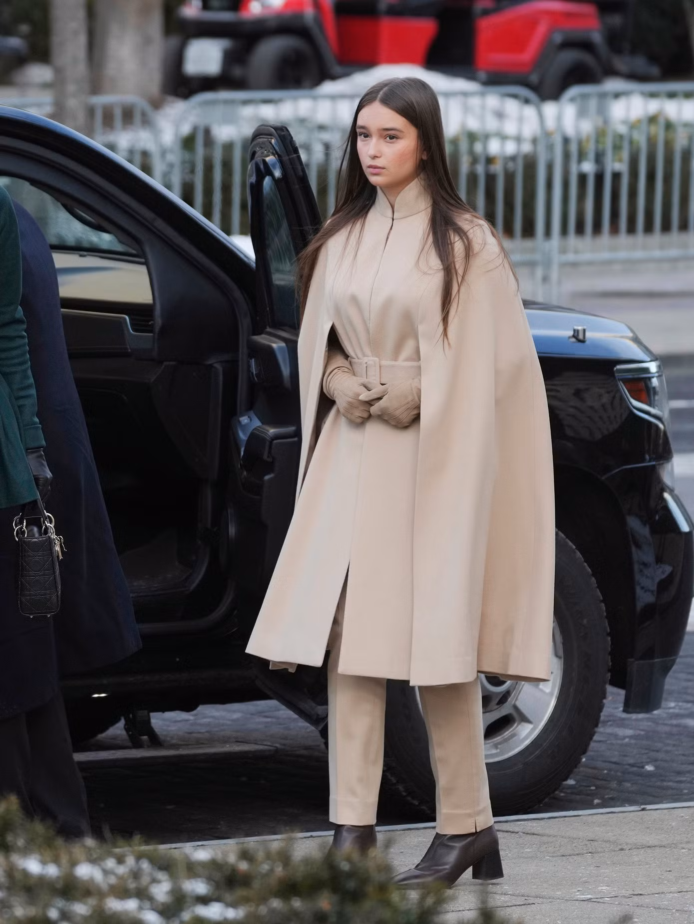 Cháu ngoại ông Trump, con gái đầu lòng 13 tuổi của Ivanka Trump - Arabella Rose Kushner chọn áo khoác chẽn dài đến đầu gối màu be, thắt lưng dày cùng màu ở eo. Chiếc áo khoác có cổ Mandarin và được phối với quần cùng màu, đôi ủng da đen có gót vuông. Trang phục của cô thiếu niên mang phong cách đồng điệu, tương tự vẻ ngoài của mẹ.
