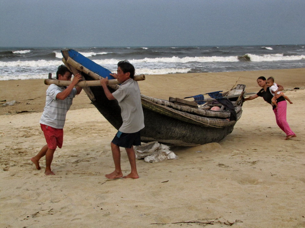 Phụ nữ bồng con nhỏ cũng ra bãi biển giúp người nhà đẩy thuyền lên cao. Ảnh: Ngọc Văn. Phụ nữ bồng con nhỏ cũng ra bãi biển giúp người nhà đẩy thuyền lên cao. Ảnh: Ngọc Văn