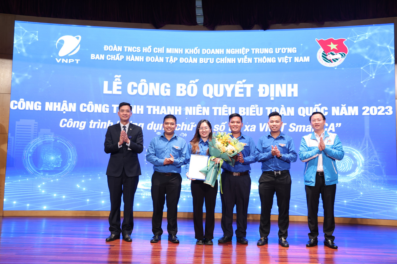Anh Trần Hữu - Trưởng Ban Thanh niên Công nhân và Đô thị T.Ư Đoàn (ngoài cùng, bên phải) trao Quyết định và ông Nguyễn Nam Long - Ủy viên BTV Đảng ủy, Phó Tổng giám đốc Tập đoàn (ngoài cùng, bên trái) tặng hoa cho nhóm tác giả Công trình thanh niên “Ứng dụng chữ ký số từ xa VNPT SmartCA”.