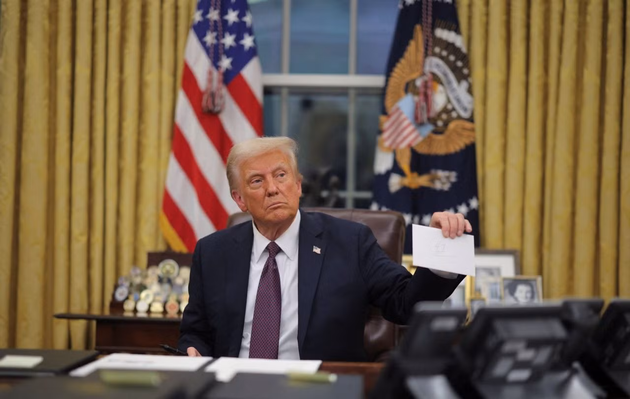 Ông Trump cầm bức thư mà người tiền nhiệm Joe Biden để lại cho ông trên bàn làm việc. Nội dung bức thư không được tiết lộ. (Ảnh: Reuters)