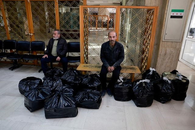 Hai người đàn ông ngồi giữa những bọc tiền mặt gần Ngân hàng Trung ương Syria sau khi chính quyền của cựu Tổng thống Bashar al-Assad sụp đổ. (Ảnh: Reuters)