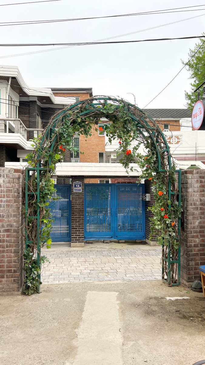 Cổng quán hiện tại, hoa đăng tiêu đã tàn nhiều, nhìn từ phía trong ra, sẽ thấy đối diện là chiếc cổng xanh dương quen thuộc - nhà của Sun Jae.