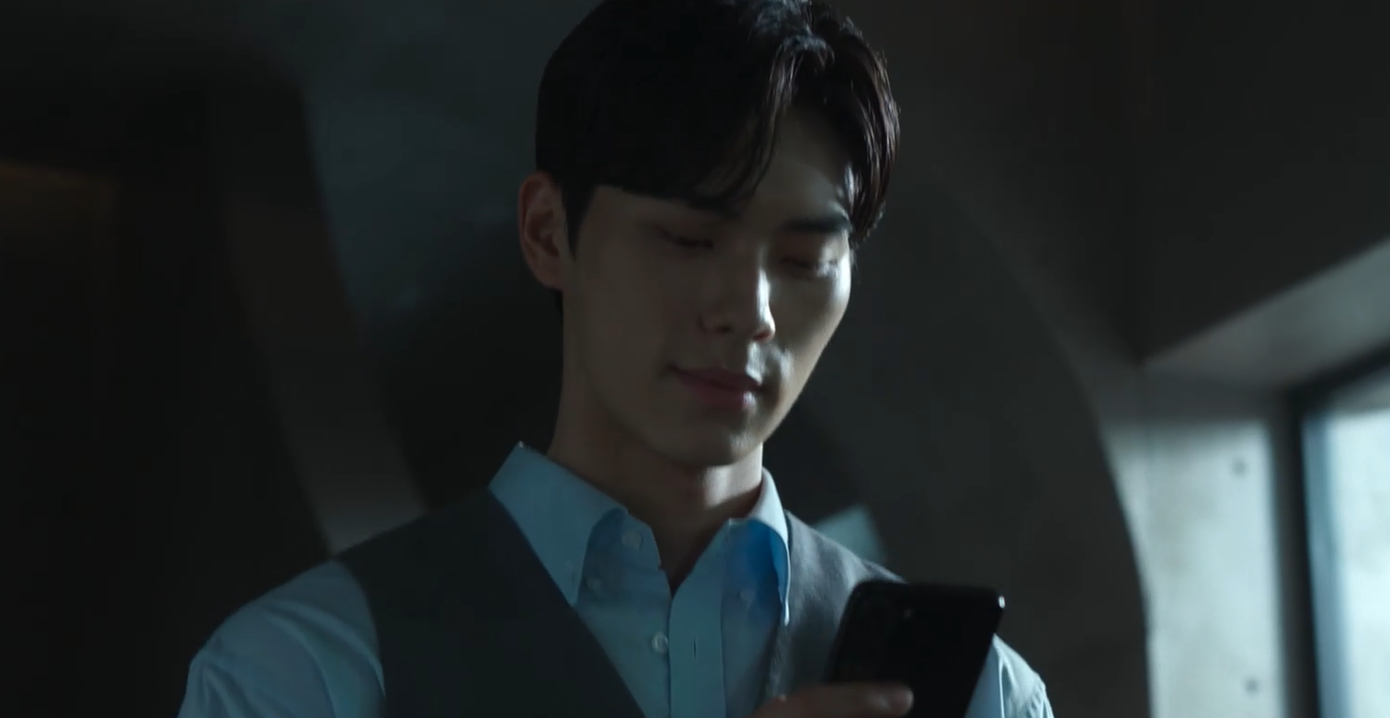 Kang Ha (Lee Chae Min) vừa cười vừa bước đi đắc ý ở hành lang và nhìn vào điện thoại.