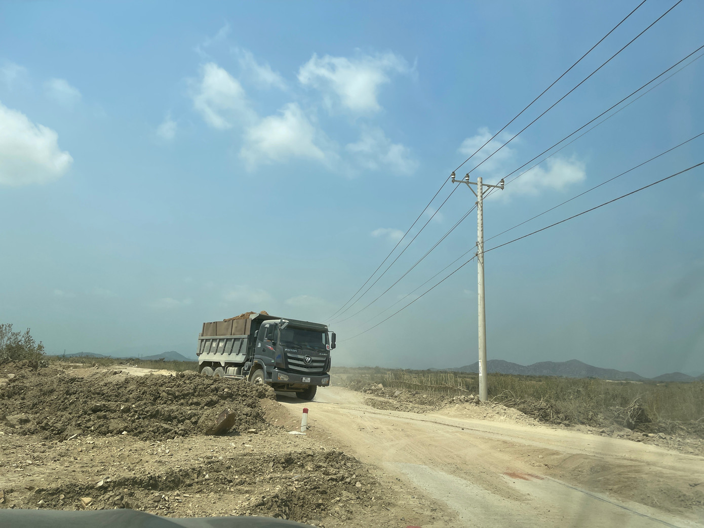 Xe tải cơi nới thùng chở vật liệu thi công cao tốc chạy trên đường giao thông nông thôn.