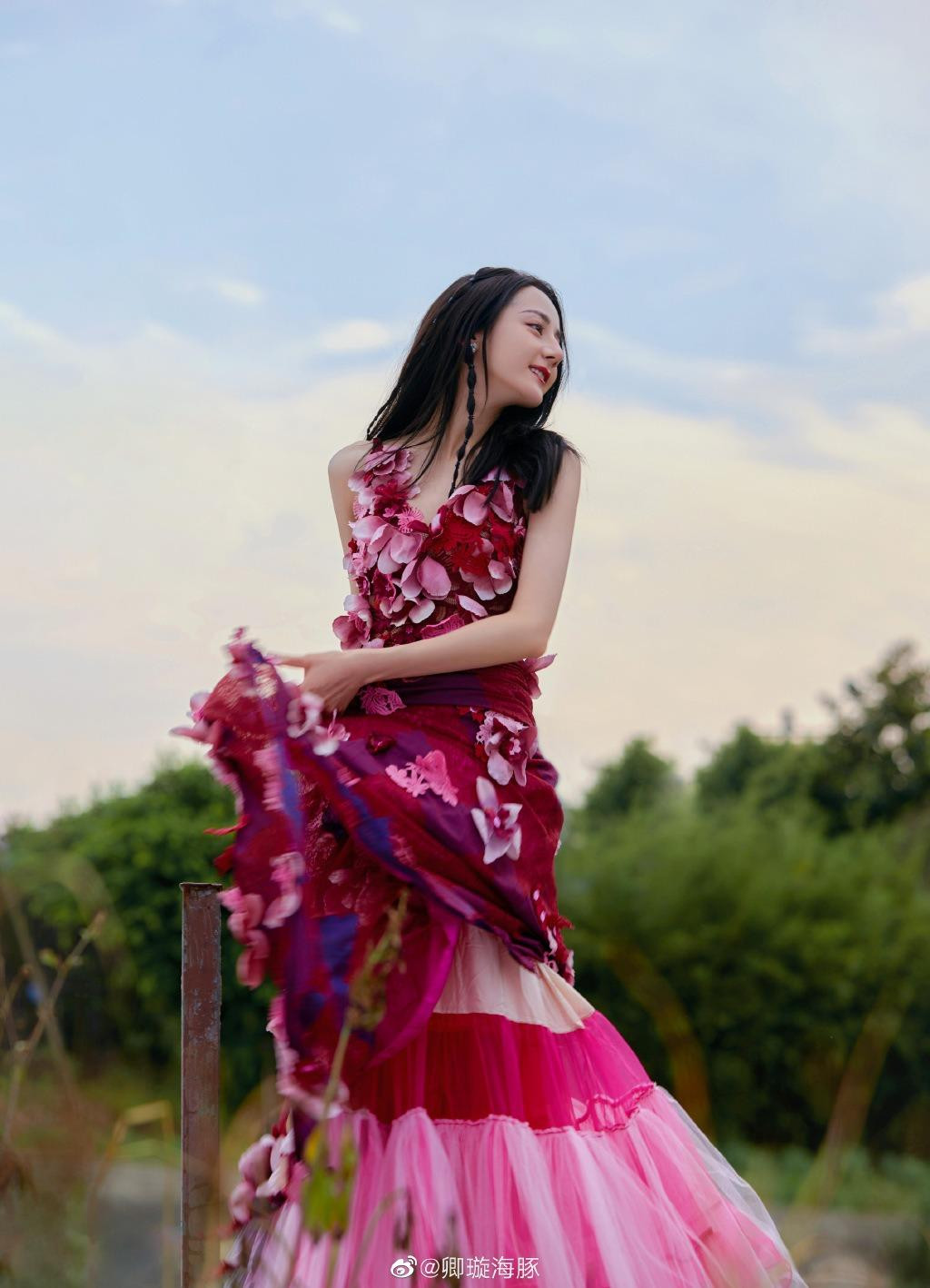 Trong ảnh, Nhiệt Ba mặc váy maxi hồng - đỏ đính hoa rực rỡ, nổi bật giữa thiên nhiên