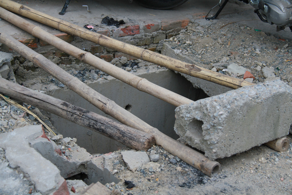 Một hố ga chưa có nắp đậy bên đường được cảnh báo bằng vài thanh tre mục nát. Ảnh: Trường Phong