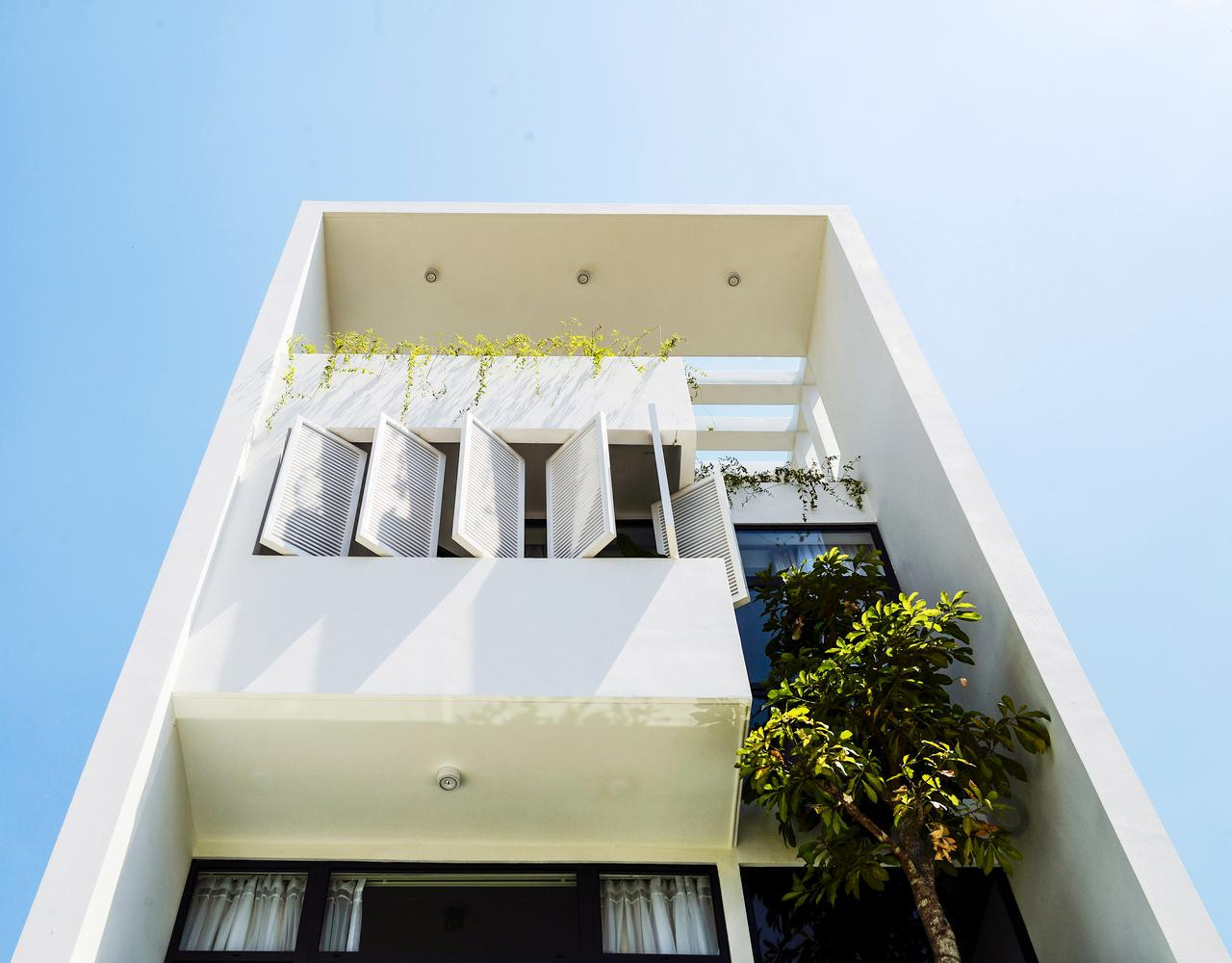 Thiết kế mặt tiền có phần hộp nhô ra, ở giữa bố trí các cửa sổ nhỏ xếp so le, bên cạnh đó là cây cao che lấp một phần mặt tiền tầng 2 và 3, tạo điểm nhấn giữa khối công trình màu trắng. Thiết kế mặt tiền có phần hộp nhô ra, ở giữa bố trí các cửa sổ nhỏ xếp so le, bên cạnh đó là cây cao che lấp một phần mặt tiền tầng 2 và 3, tạo điểm nhấn giữa khối công trình màu trắng.