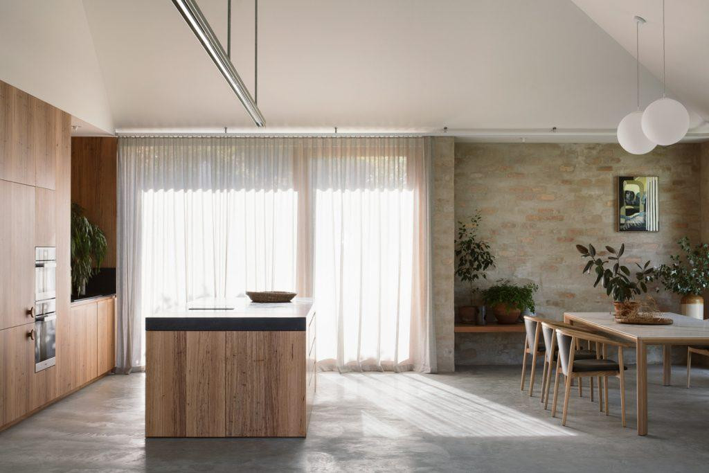 Các thiết bị chiếu sáng treo lơ lửng, bao gồm một mặt dây chuyền tuyến tính phía trên đảo bếp, làm nổi bật cảm giác về chiều cao trong các khu vực sinh hoạt.