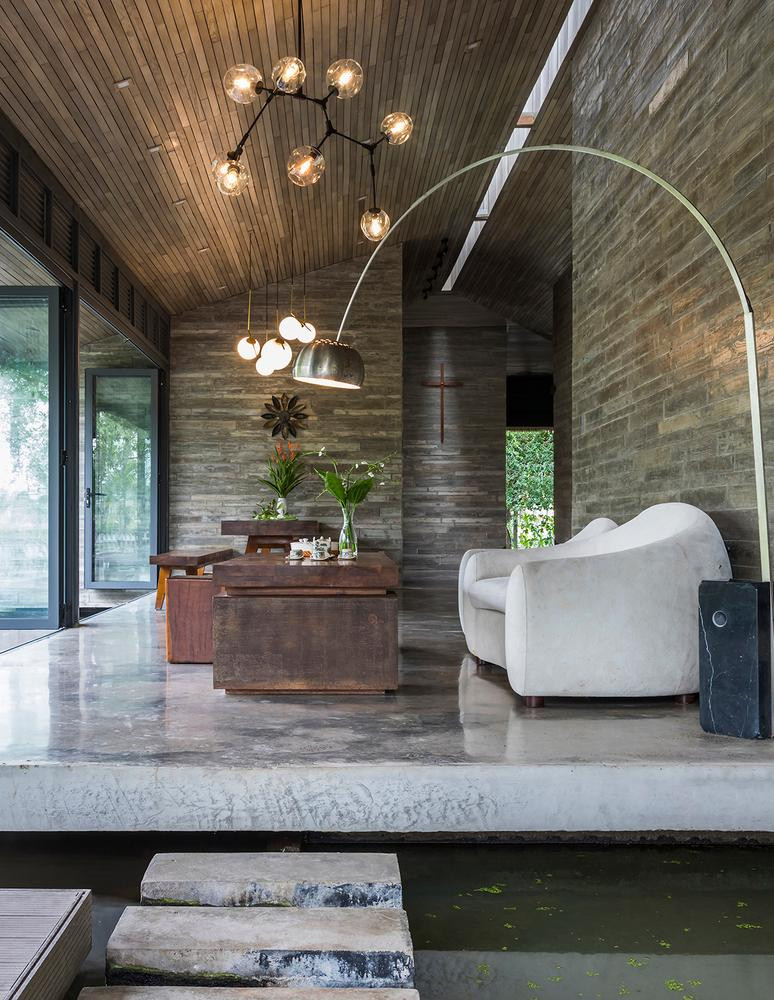 Hệ thống trần gỗ cùng màu với tường bê tông lót gỗ (ván bê tông vân gỗ thủ công) để tạo ra sự đồng điệu về màu sắc không gian. Trong hình là không gian phòng khách.