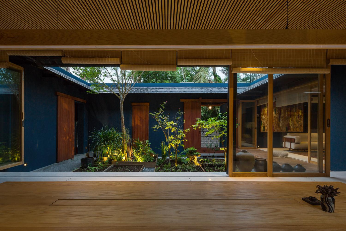 Các cửa trong nhà đều bằng kính có thể đóng ra mở vào giúp ngôi nhà luôn thông thoáng và tràn ngập ánh sáng tự nhiên. Ở giữa nhà là khu vườn với nhiều cây xanh cung cấp oxy và sinh khí cho người ở. Bên cạnh đồ nội thất bằng gỗ, mây, tre, gia chủ còn ưu tiên sử dụng thảm thổ cẩm kết hợp với màu xanh xám của các bức tường tạo nên một không gian mang đậm phong cách vintage. Ngoài cửa kính, ngôi nhà còn sử dụng rèm che bằng trúc để giảm sự chói chang của ánh sáng vào những ngày hè.