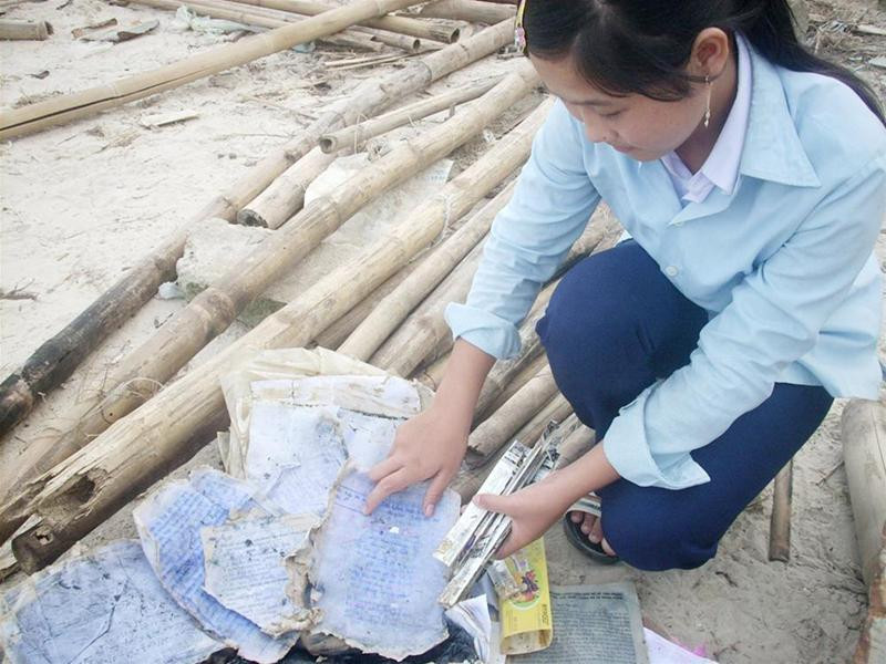 Em Trần Thị Búp bên đống sách vở lấm lem bùn đất vừa tìm thấy sau mưa bão