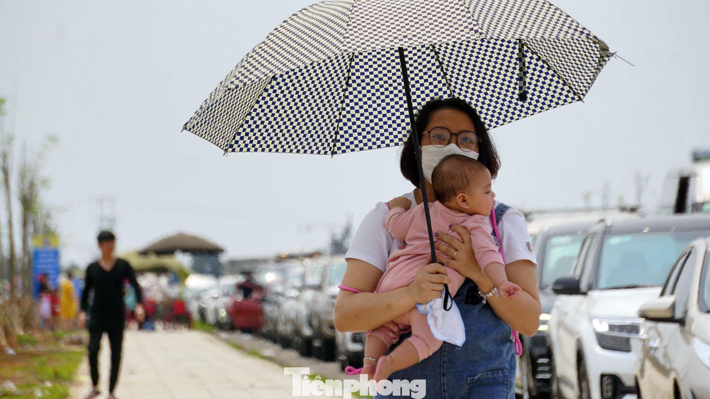Một nữ du khách bế con nhỏ rời ô tô đi bộ hàng trăm mét đến điểm chờ lên phà để tránh nóng.