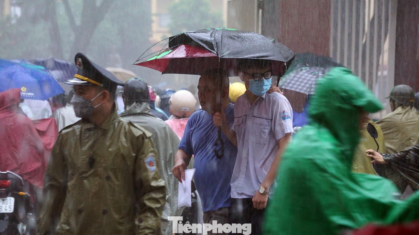 Phụ huynh và thí sinh đội mưa di chuyển qua dòng người trên phố Cát Bi (quận Hải An, Hải Phòng).