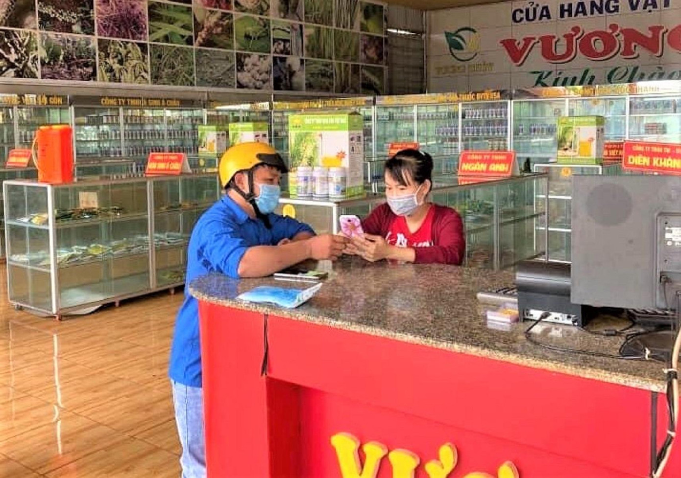 Một thanh niên hướng dẫn chủ cửa hàng sử dụng ứng dụng Bluezone Một thanh niên hướng dẫn chủ cửa hàng sử dụng ứng dụng Bluezone