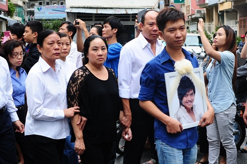 Mẹ của Wanbi (áo đen) lặng lẽ đi sau di ảnh của anh. Kể từ khi Wanbi trút hơi thở cuối cùng, bà đã cố gắng gồng mình để cùng anh Tùng - quản lý của nam ca sĩ - lo chu toàn mọi chuyện trong tang lễ