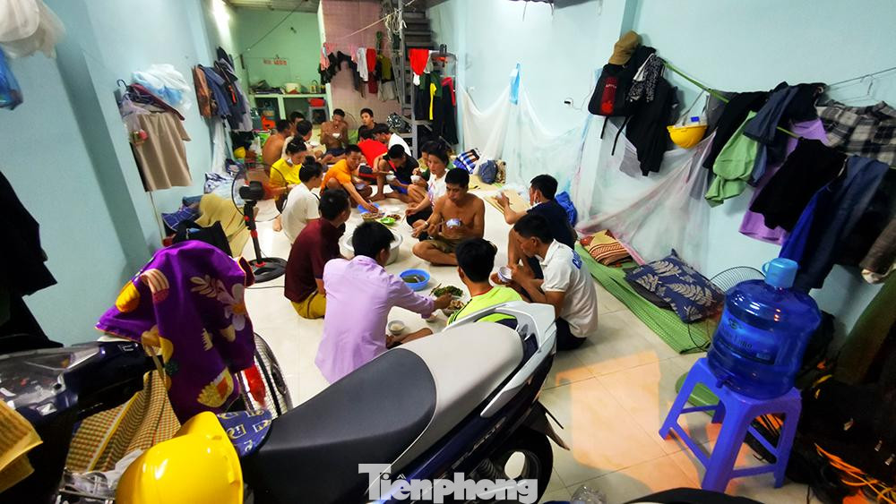 Hơn 20 người ngồi ăn tối dưới sàn nhà. Đây cũng là không gian sinh hoạt chung từ sáng đến khi đi ngủ của những công nhân xây dựng này.