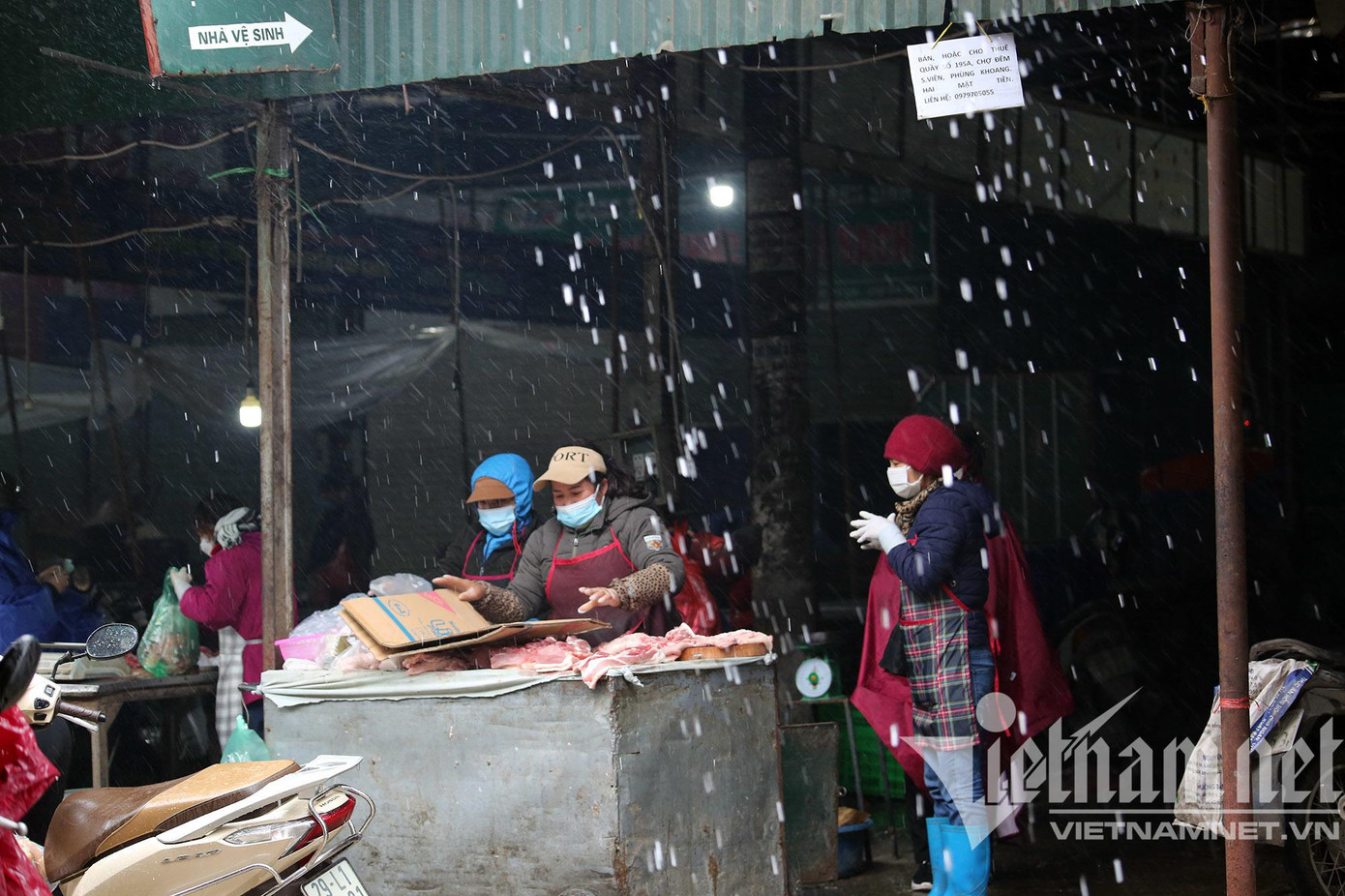 Quầy hàng thịt ở chợ Phùng Khoang che chắn giữa những trận mưa rào trong ngày 19/2. Chủ các sạp hàng đều trong trang phục chống rét, áo choàng, mũ len, gang tay khi thường xuyên tiếp xúc với nước lạnh.