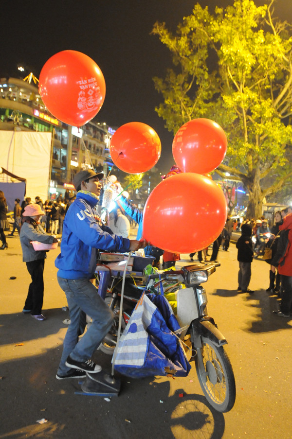 Anh Đức cùng vợ - chị Hằng (quê ở Hoằng Hóa, Thanh Hóa) đêm giao thừa vẫn gắng sức đẩy xe quanh Hà Nội bán bỏng ngô và bóng bay. Anh cho biết, hơn 10 năm rồi anh chưa ăn tết ở nhà. Năm nay, sau khi thu hoạch vụ hè thu, hai vợ chồng anh lại dắt nhau ra Hà Nội làm thêm. Anh cho biết, cùng ngày này năm ngoái, vợ chồng anh bán được tới ba triệu đồng, tuy nhiên, đêm 29 này anh chỉ bán được một triệu. Nếu hết đêm nay kiếm được vài triệu, anh chị sẽ bắt xe về luôn với hai con đang ở quê cùng ông bà. Tuy nhiên, nếu được ít, anh chị sẽ ở lại làm thêm tới rằm tháng giêng mới về quê.