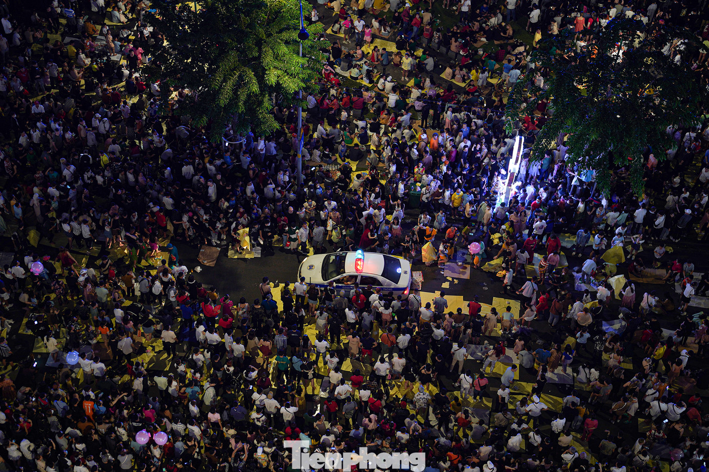 Một chiếc ô tô của lực lượng chức năng vất vả mở đường qua khu vực người dân ngồi đợi xem pháo hoa.