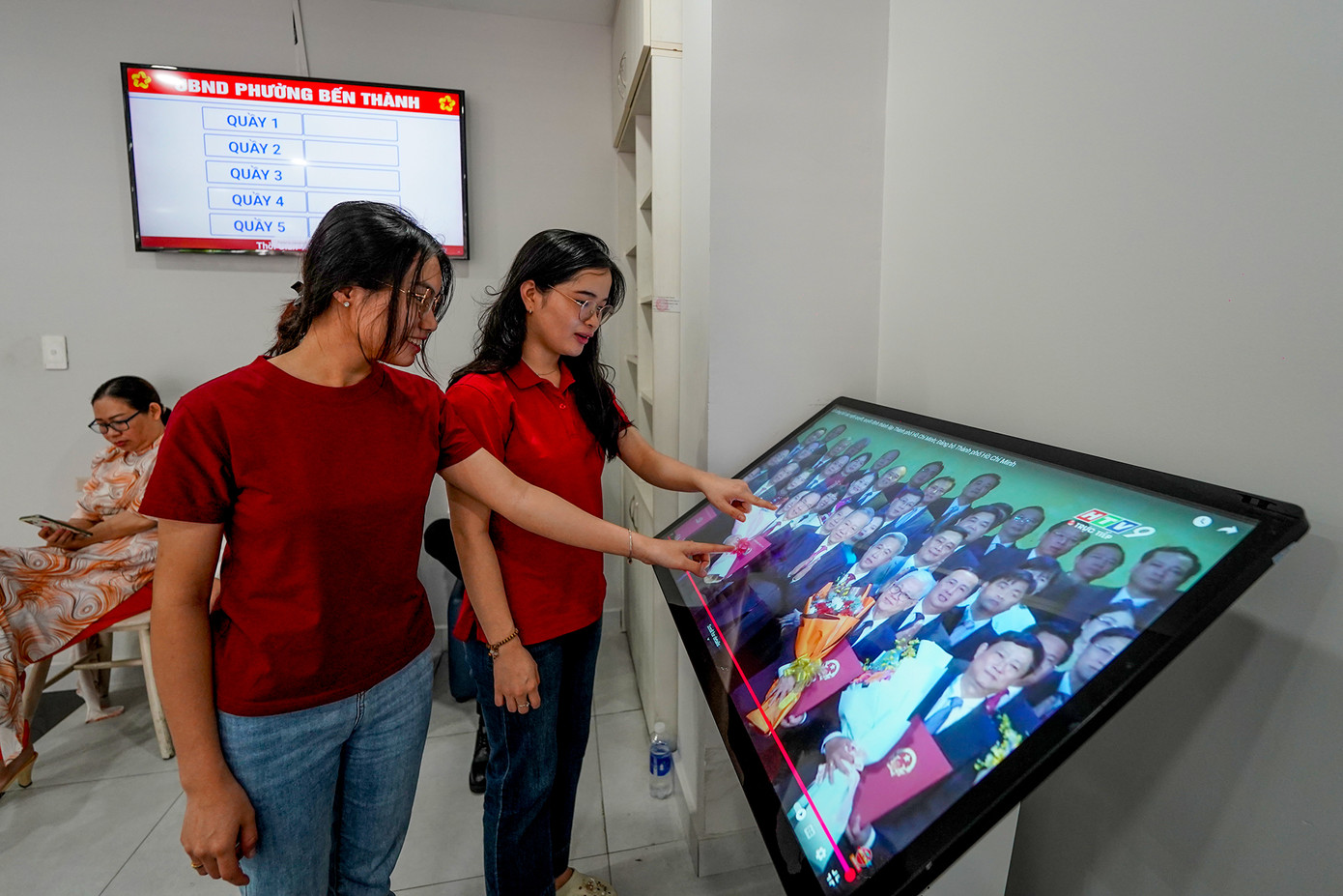 Người dân theo dõi lễ công bố các nghị quyết, quyết định của Trung ương và địa phương về sáp nhập đơn vị hành chính TPHCM mới qua màn hình cảm ứng khi đến phường Bến Thành làm thủ tục.