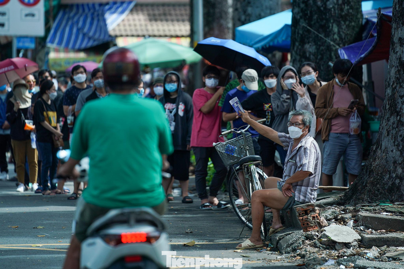 Một phe vé đang ngồi chào mời người đi đường trước những người đứng xếp hàng.