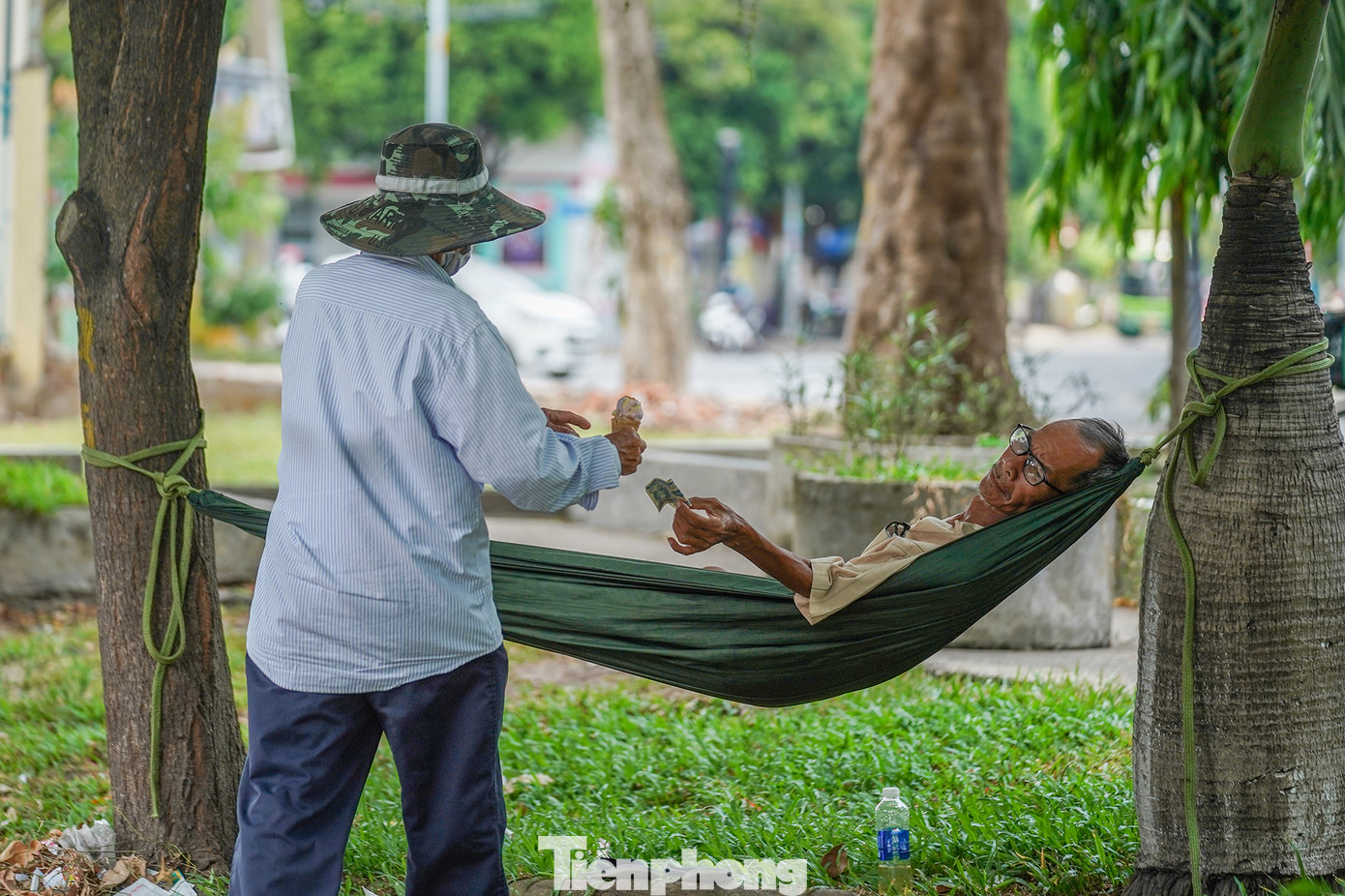 Một người dân mắc võng trong công viên để tránh nóng. Tuy đã chuẩn bị nước đầy đủ nhưng ông cũng phải mua thêm một cây kem để giải nhiệt.