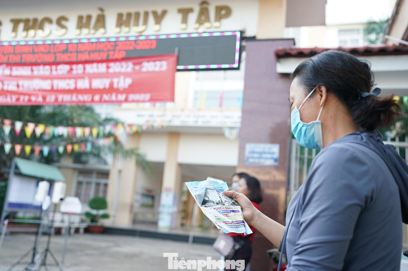 Phía bên ngoài điểm thi, một phụ huynh đợi con và tham khảo thông tin tuyển sinh của một số trường.