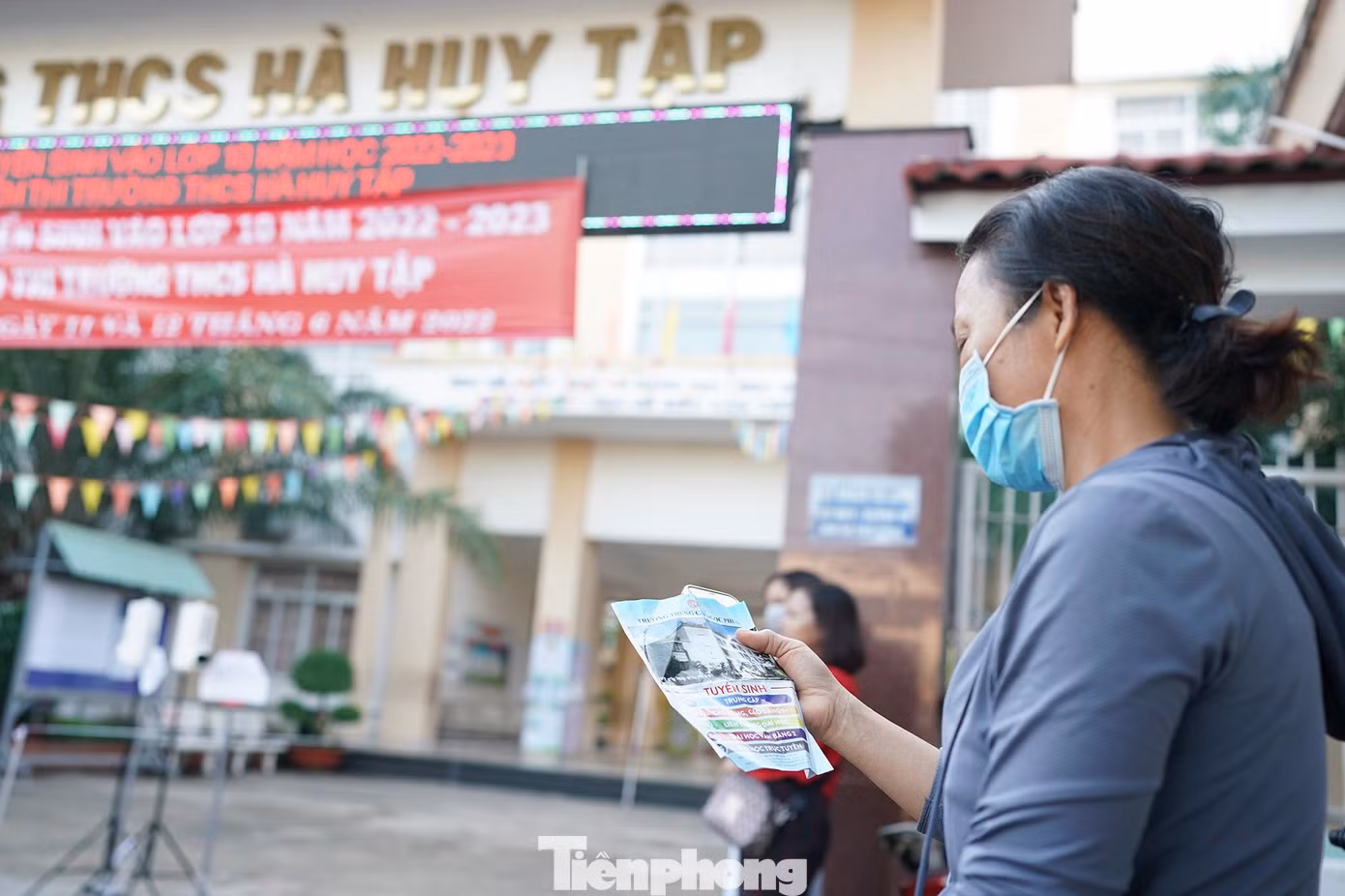 Phía bên ngoài điểm thi, một phụ huynh đợi con và tham khảo thông tin tuyển sinh của một số trường.