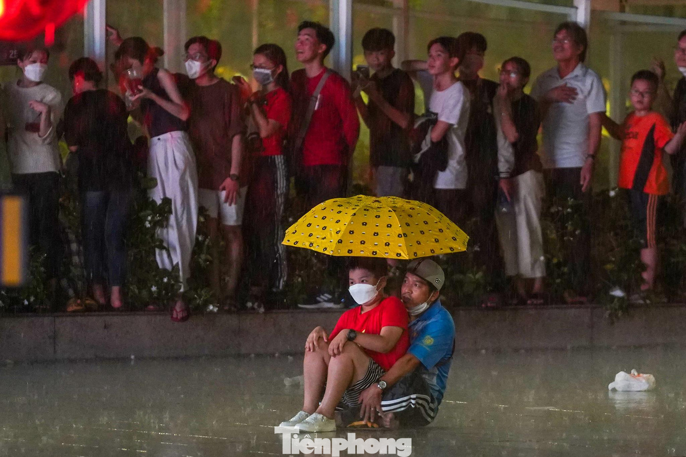 Hai bố con này vì không còn chỗ đứng tránh mưa nên đành ngồi theo dõi luôn trong chiếc ô. Hai bố con này vì không còn chỗ đứng tránh mưa nên đành ngồi theo dõi luôn trong chiếc ô.