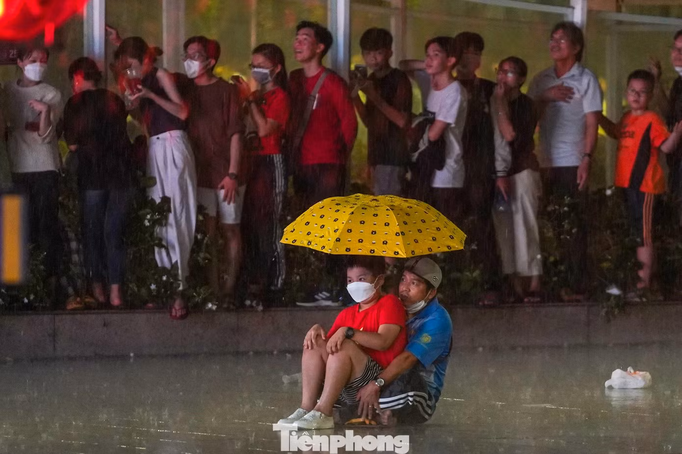 Hai bố con này vì không còn chỗ đứng tránh mưa nên đành ngồi theo dõi luôn trong chiếc ô.