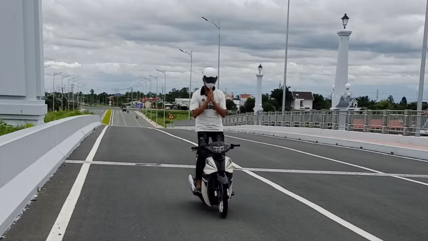 L. biểu diễn chạy xe buông tay, đứng trên xe, biểu diễn tư thế chấp tay vái lạy trên cầu Bảo Định (đường Vành đai TP Tân An). (Ảnh: CA)