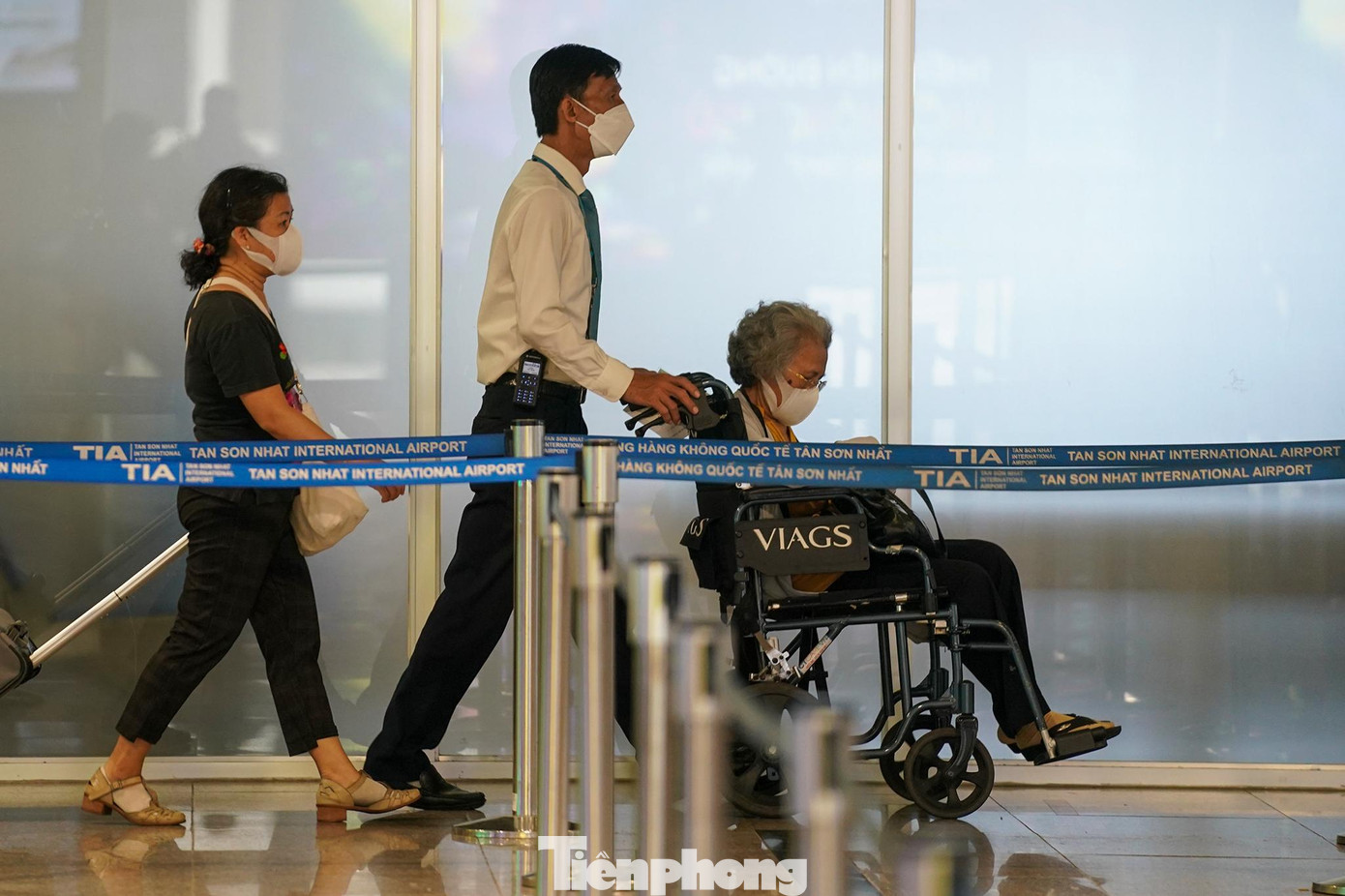 Nhân viên dịch vụ mặt đất đang hỗ trợ xe lăn cho khách cao tuổi tại một lối đi khá thông thoáng.