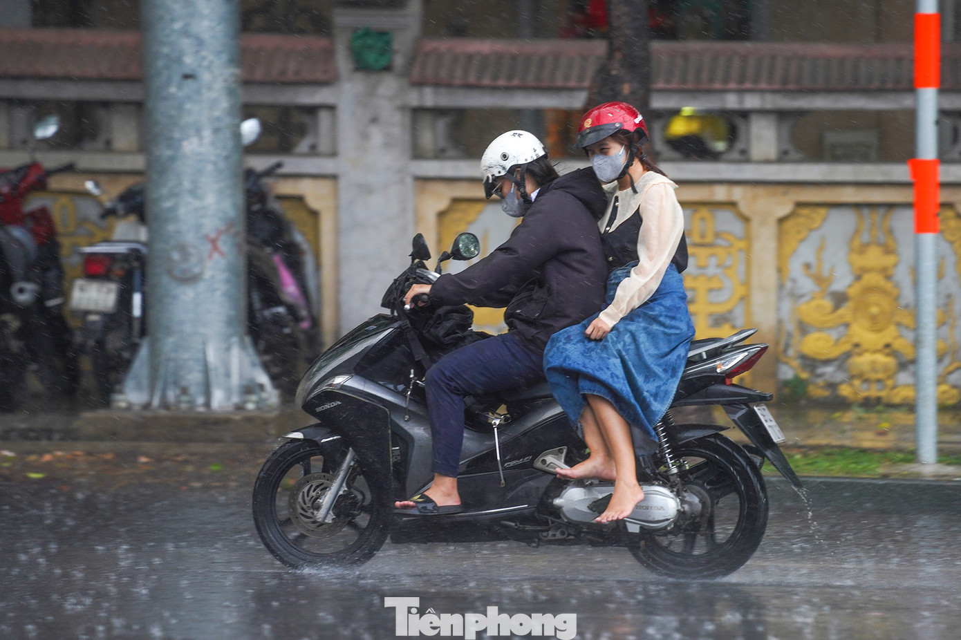 Một người phụ nữ cất giày vì gặp cơn mưa bất chợt, trong khi trên người vẫn còn quấn chiếc khăn chống nóng.