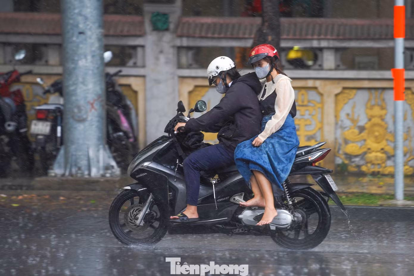 Một người phụ nữ cất giày vì gặp cơn mưa bất chợt, trong khi trên người vẫn còn quấn chiếc khăn chống nóng.