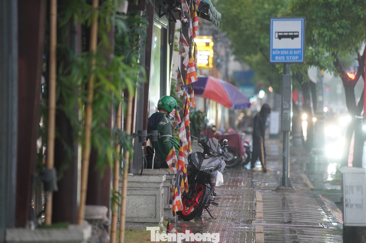 Một tài xế xe ôm công nghệ trú vội dưới mái hiên để tránh mưa .