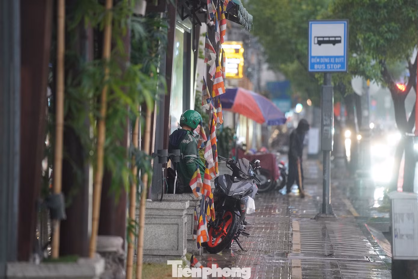 Một tài xế xe ôm công nghệ trú vội dưới mái hiên để tránh mưa .