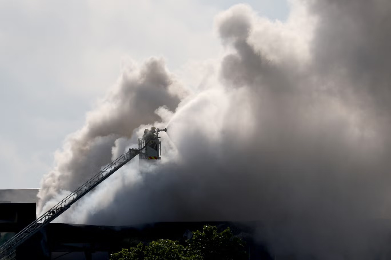 Các thành viên của đội cứu hộ khẩn cấp trên một bục được nhìn thấy như những cột khói từ một tòa nhà lưu trữ các sản phẩm vệ sinh hồ bơi, tại thành phố ven biển Vilanova i la Geltru, phía nam Barcelona vào ngày 10/5.