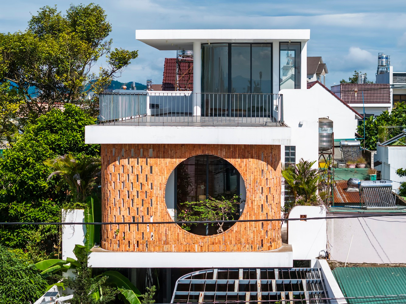 Cửa sổ tròn lớn ở tầng trên là điểm nhấn chính của mặt tiền, không chỉ đóng vai trò là chi tiết thẩm mỹ mà còn là sự kết nối giữa ngôi nhà và môi trường xung quanh, mang đến tầm nhìn thoáng đãng và ánh sáng tự nhiên cho nội thất.