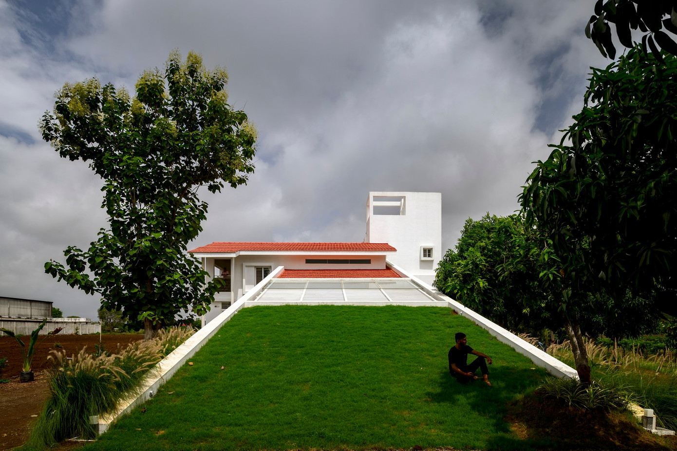 Nhìn từ mặt tiền thẳng về phía Đông, bãi cỏ dốc dần kết nối với bóng râm của giàn che, rồi cuối cùng đạt đến đỉnh cao là mái dốc ngói Mangalore truyền thống.