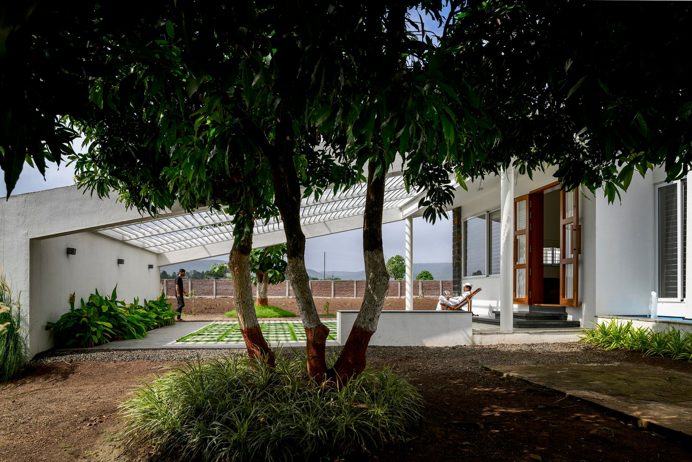 Nhìn từ mặt tiền thẳng về phía Đông, bãi cỏ dốc dần kết nối với bóng râm của giàn che, rồi cuối cùng đạt đến đỉnh cao là mái dốc ngói Mangalore truyền thống.