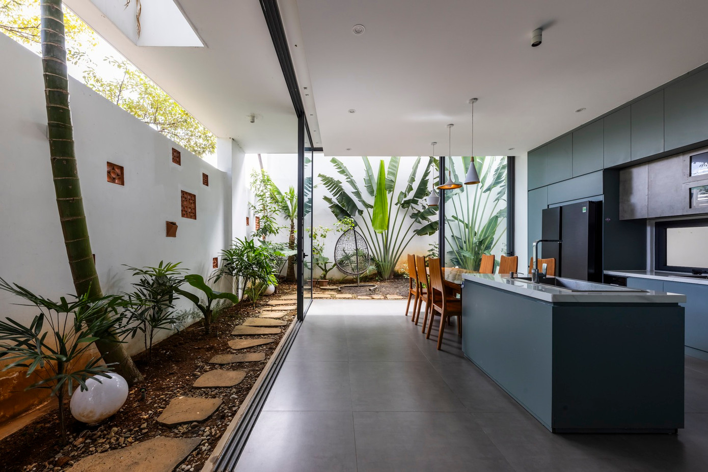 Bên ngoài là một khu vườn nhỏ tươi tốt, nơi gia đình có thể thưởng thức bữa ăn ngoài trời hoặc hít thở không khí trong lành. Sự kết hợp giữa ánh sáng tự nhiên, cây xanh và vật liệu tự nhiên tạo nên không gian sống mở kết nối con người với thiên nhiên.