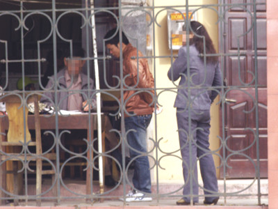 Trong khuôn viên của Phòng PA61, cò L (X) đang ghi tờ khai sau khi đã thỏa thuận với khách. Người phụ nữ đứng bên cạnh cũng là một cò quen thuộc với nhiều người dân đến làm thủ tục cấp hộ chiếu. Ảnh chụp sáng 31-3-2011 Ảnh: N.H